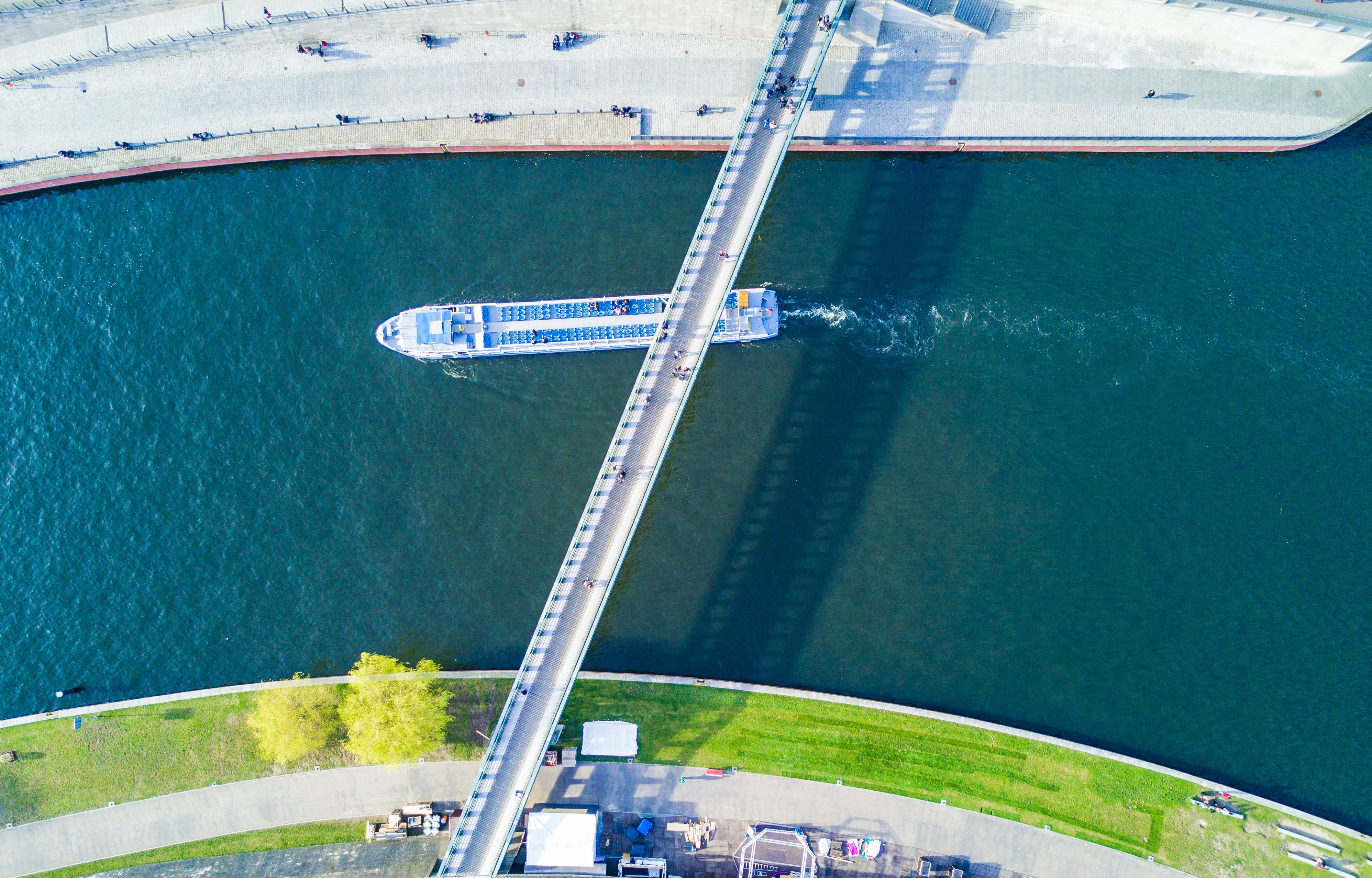 A ferry in a river under a bridge seen from above