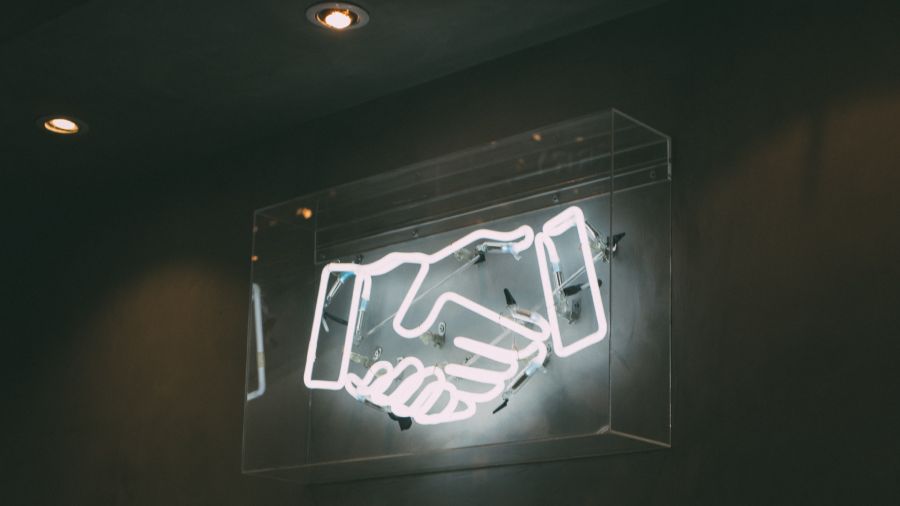 An image of a neon light with two hands shaking