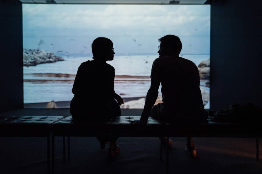 Two backlighted people talking and sitting in front of  a projector that shows a video